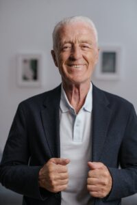 Senior man smiling confidently indoors in a black suit jacket, embodying vibrant lifestyle.